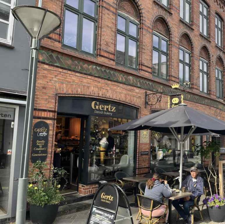 Billedet beskriver Gertz Danish Bakery. Her kan man se cafeborde med stole under en parasol
