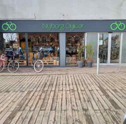 En træbro leder ind til Nyborg Cykler. Foran butikken står der cykler af alle mulig slags.